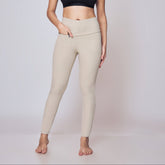 Woman wearing a black sports bra and beige leggings on a plain background