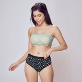 Woman wearing a light green strapless top and black patterned high-waisted shorts on a plain background