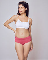 Woman wearing a white sports bra and pink high-waisted underwear on a gray background