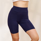 Woman wearing a white sports bra and navy blue shorts posing against a neutral background.
