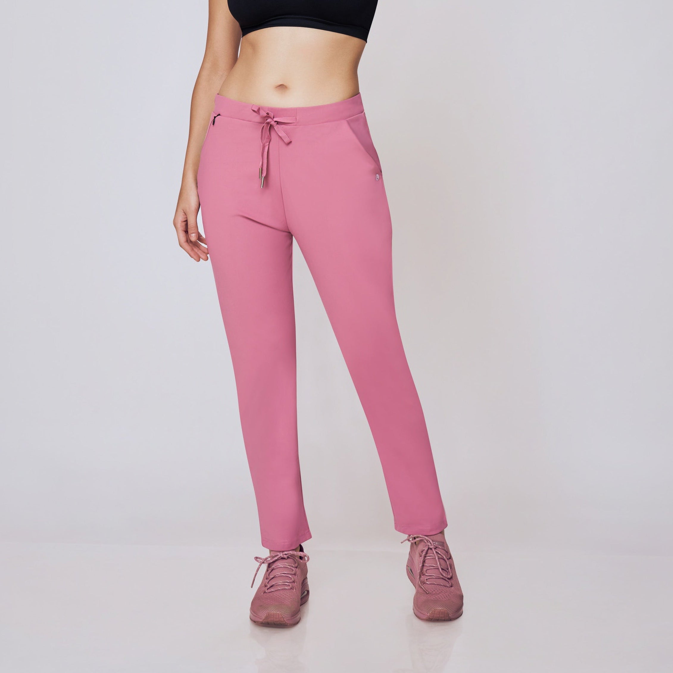 Woman wearing a black sports bra and pink pants on a white background