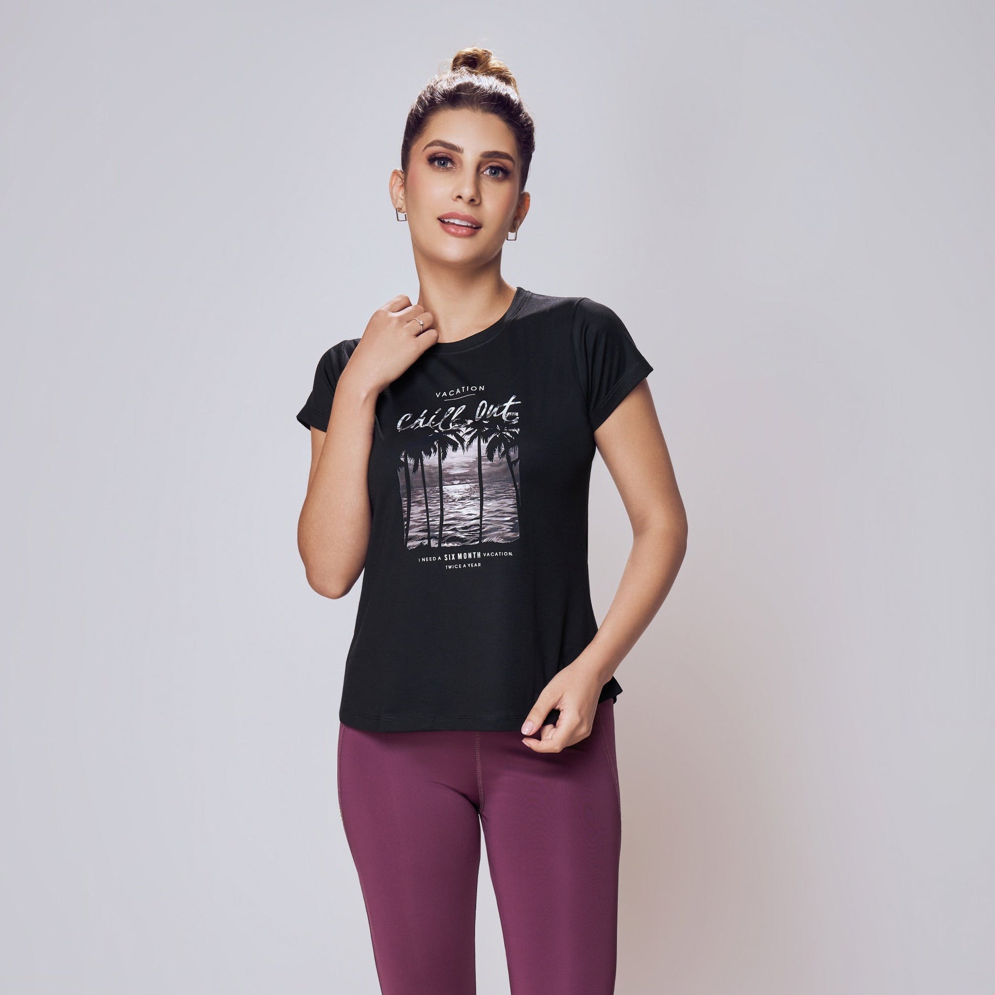 Woman wearing a black t-shirt with a graphic design and purple leggings on a white background