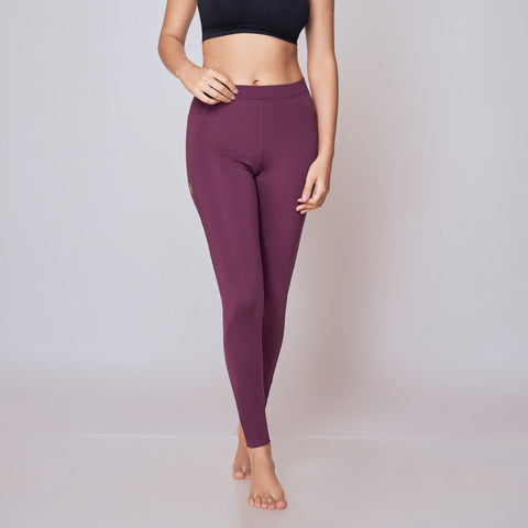 Woman wearing a black sports bra and wine leggings on a light gray background