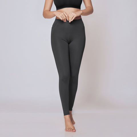 Woman wearing a black sports bra and gray active tights on a white background