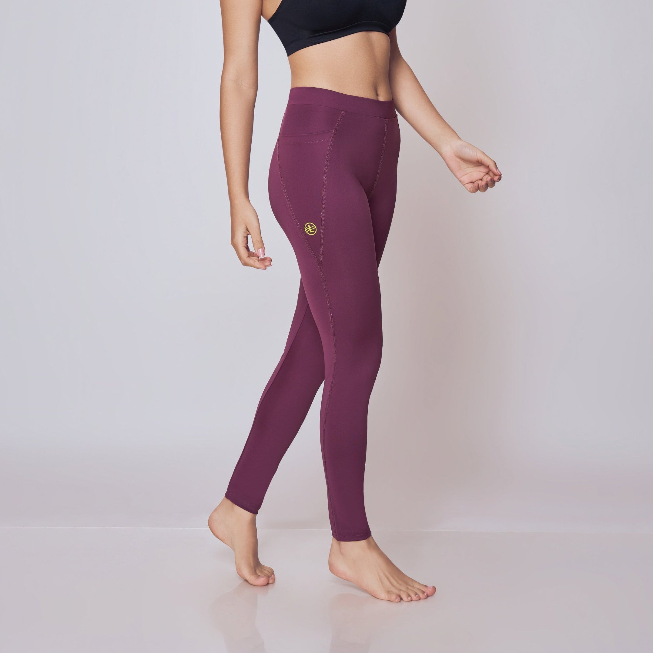 Woman wearing a black sports bra and wine leggings on a plain background