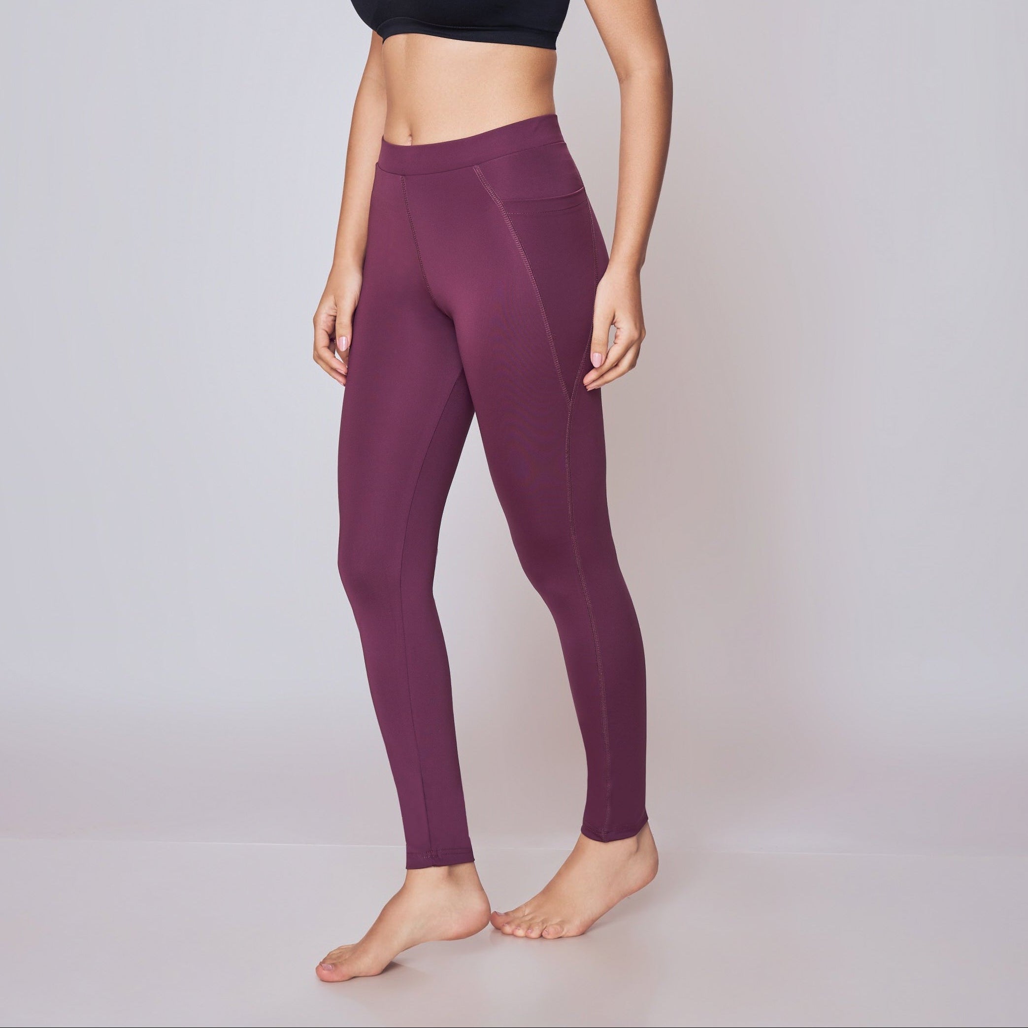 Woman wearing a black sports bra and Wine leggings on a white background