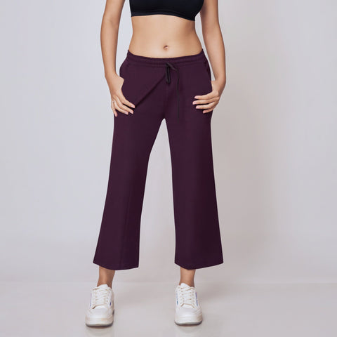 Woman wearing a black sports bra and purple Ankle Length Track Pants on a white background