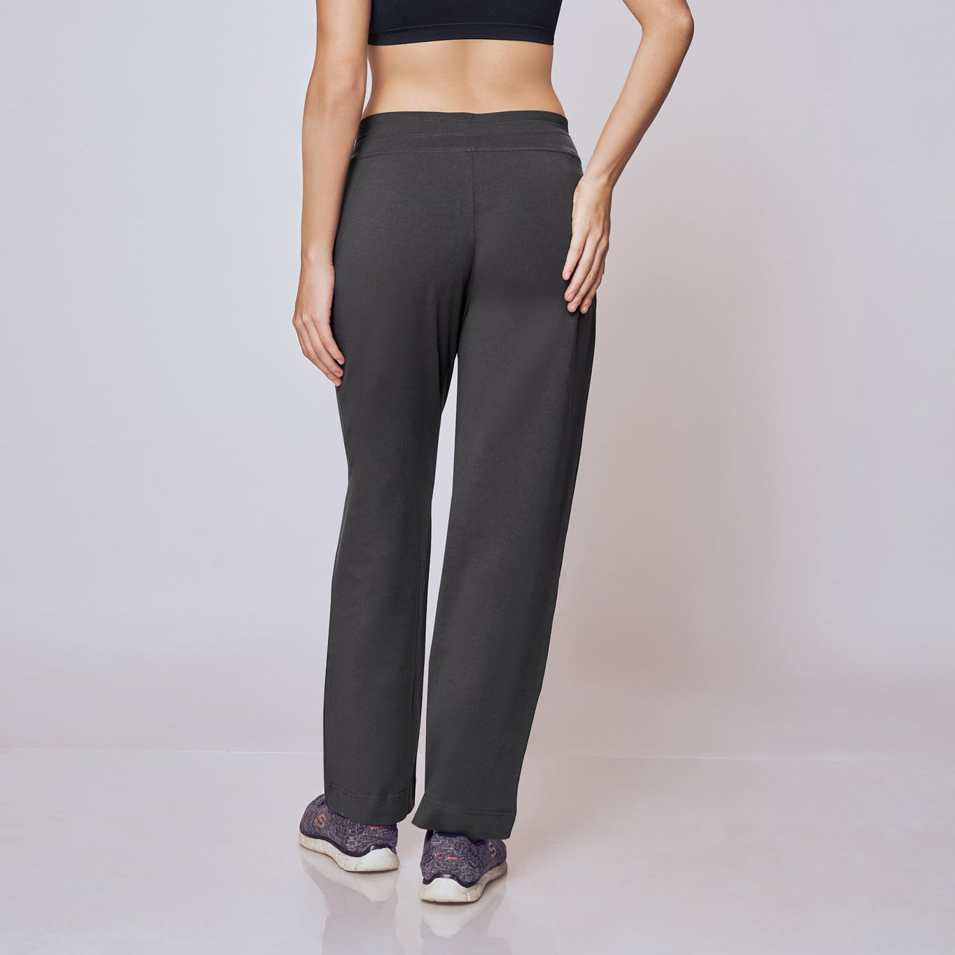 Woman wearing a black sports bra and gray Classic Flex Regular Fit Track Pants on a white background
