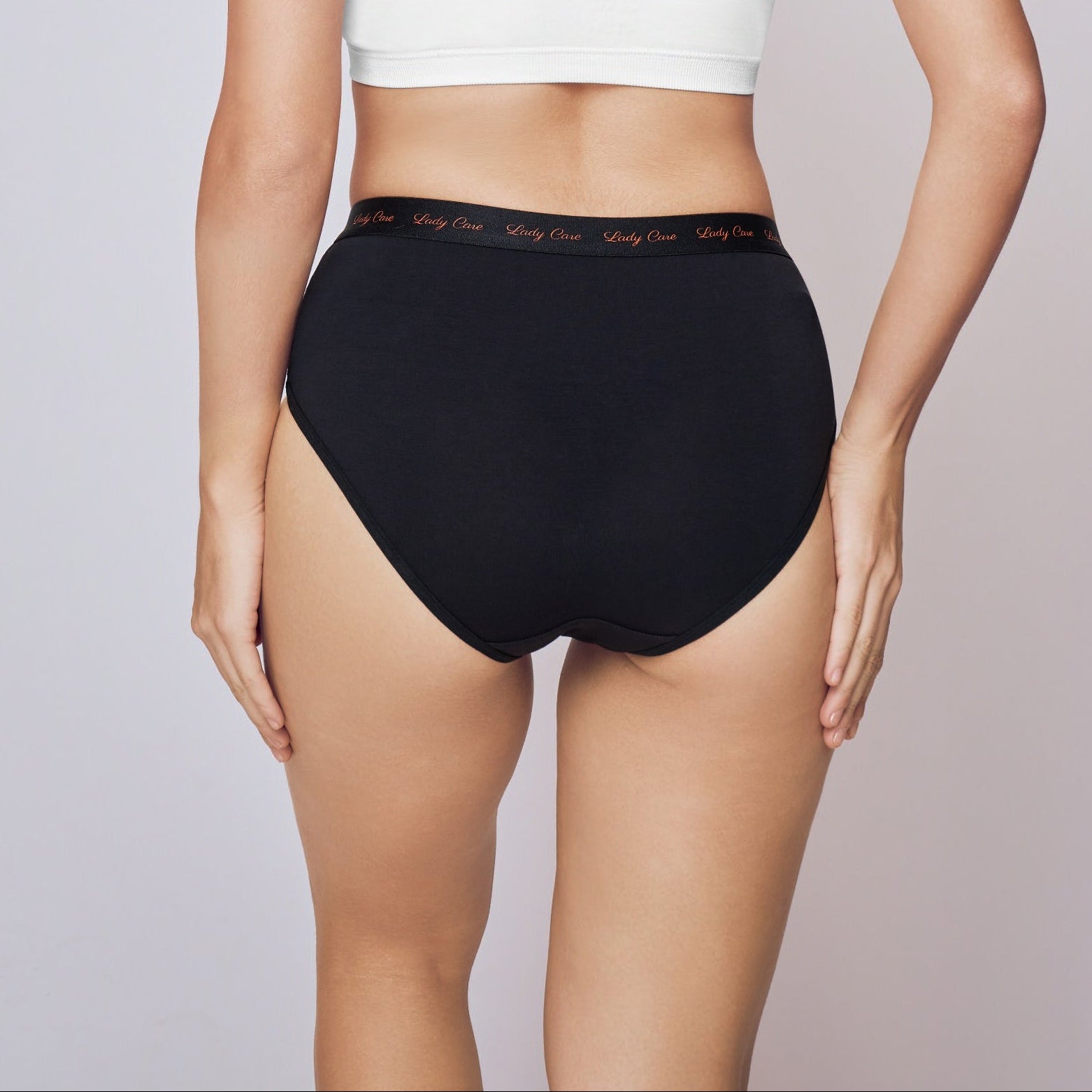 Woman wearing a white bikini top and black high-waisted bottoms on a plain background