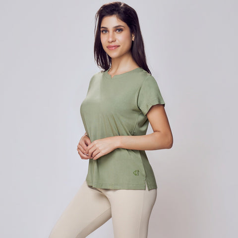 Woman wearing a green Cosy Cotton T-Shirt and beige leggings on a white background