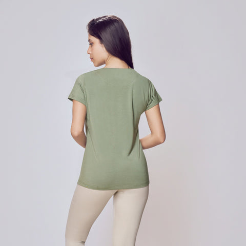 Woman wearing a green Cosy Cotton T-Shirt and beige leggings on a white background