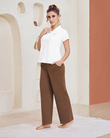 Woman wearing a white shirt and brown Cosy Flared Track Pants standing in a modern indoor setting with geometric wall designs.