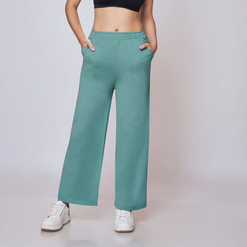 Woman wearing a black sports bra and teal pants on a plain background