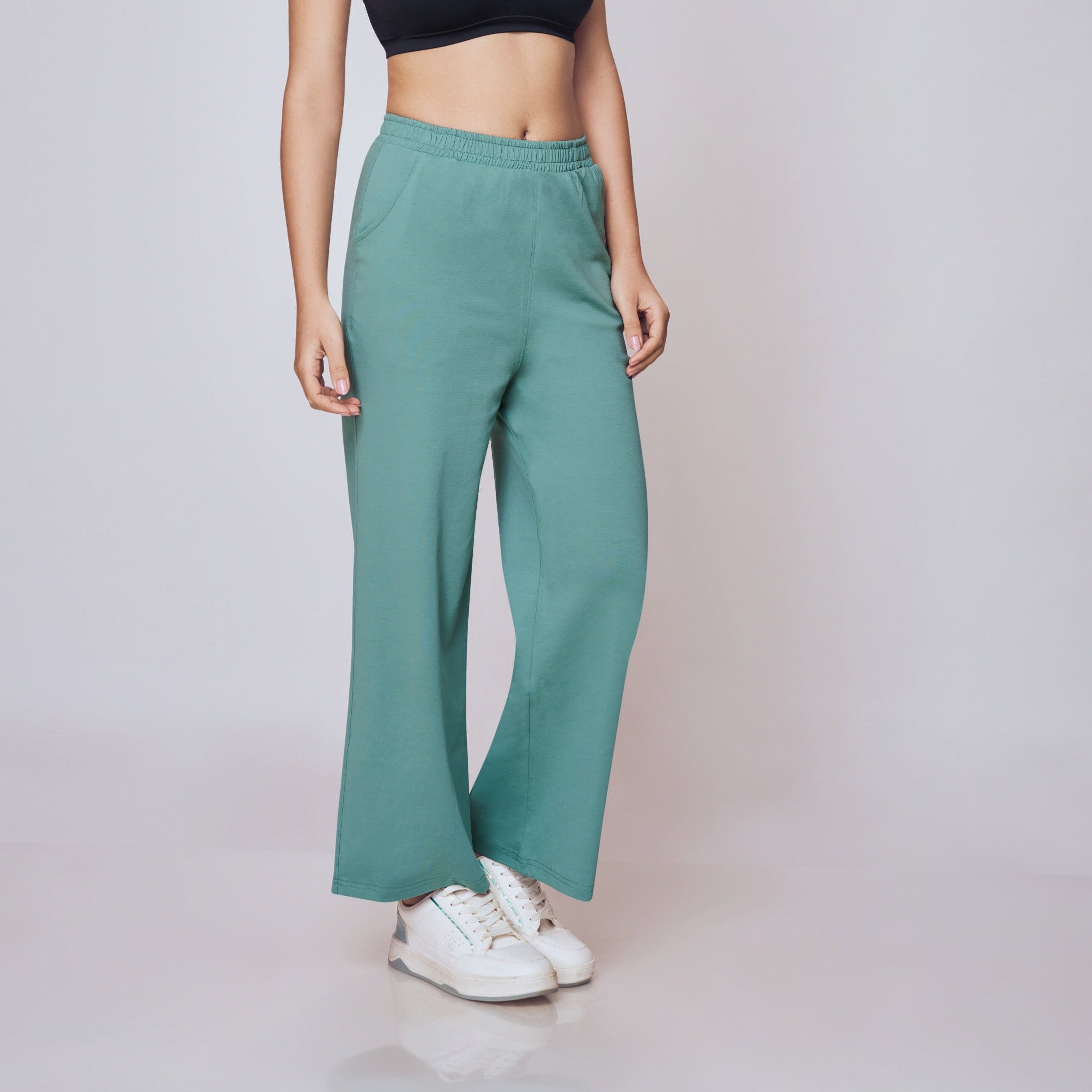 Woman wearing a black sports bra and teal pants on a white background