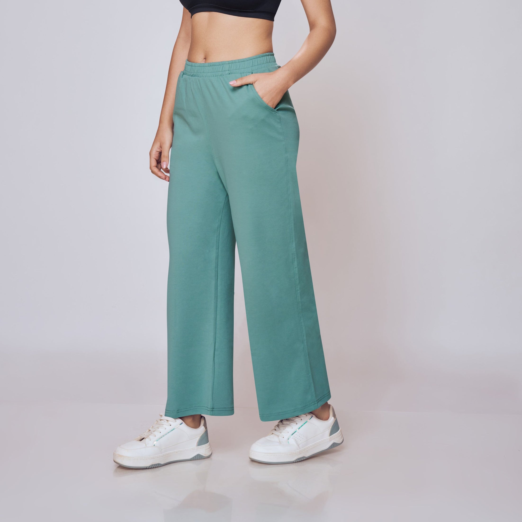 Woman wearing a black sports bra and teal pants on a light gray background