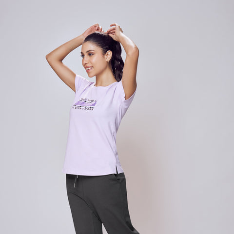 Person wearing a white t-shirt with a logo and dark pants on a light gray background