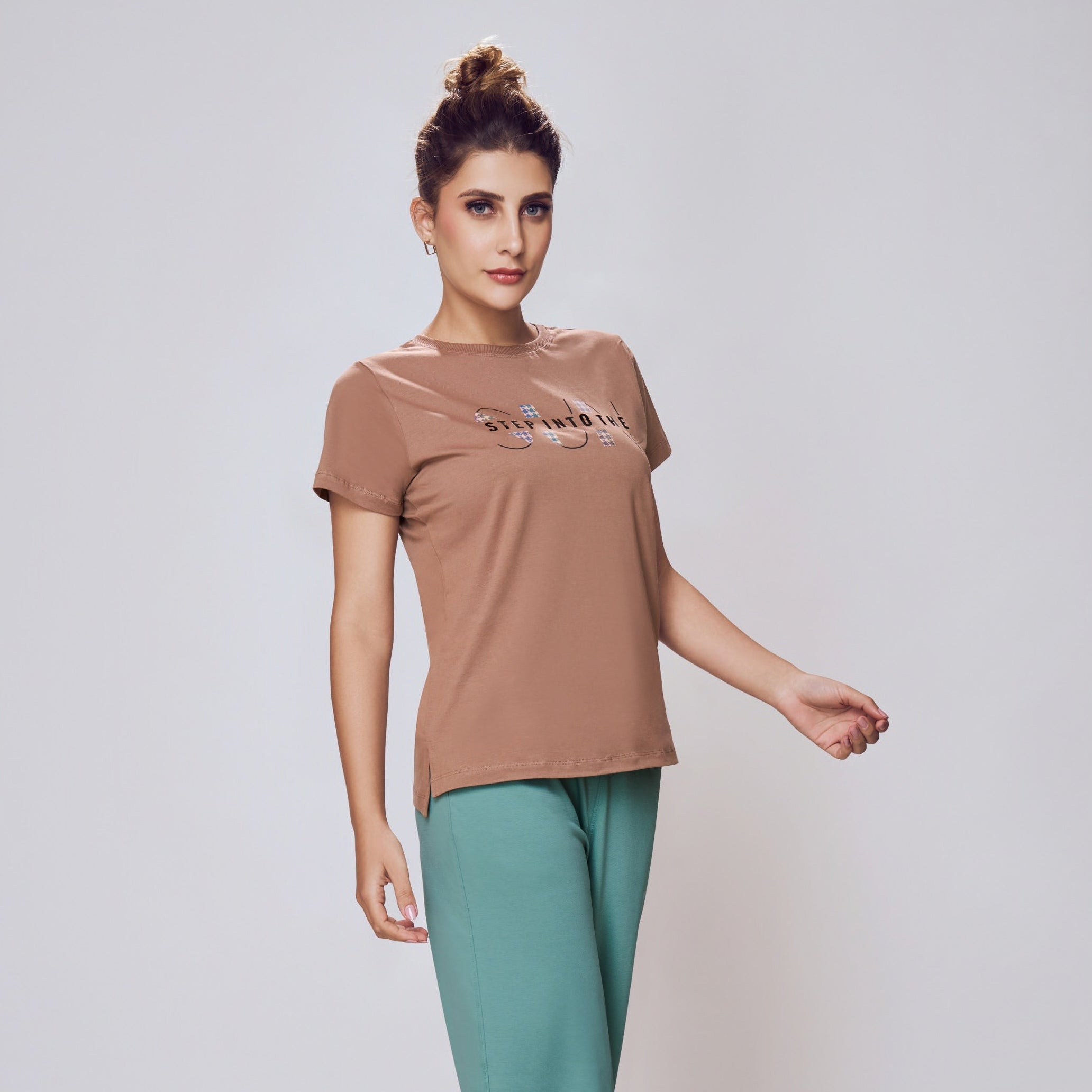Woman wearing a brown t-shirt and teal pants on a white background