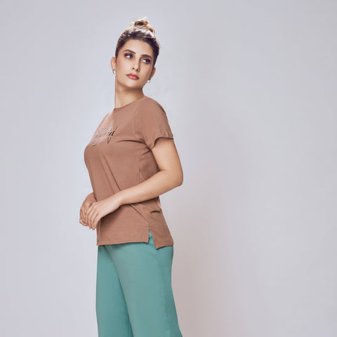 Woman wearing a brown top and teal pants on a light gray background