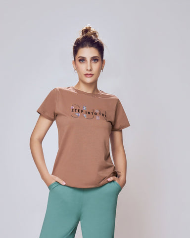 Woman wearing a brown t-shirt and teal pants on a white background