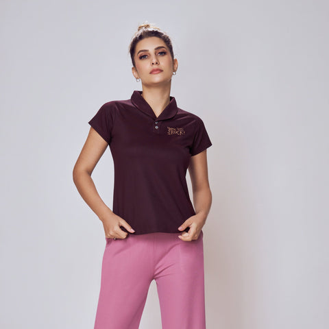 Woman wearing a dark purple polo shirt and pink pants on a white background