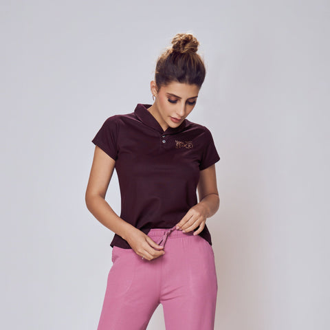 Woman wearing a dark purple polo shirt and pink pants on a white background