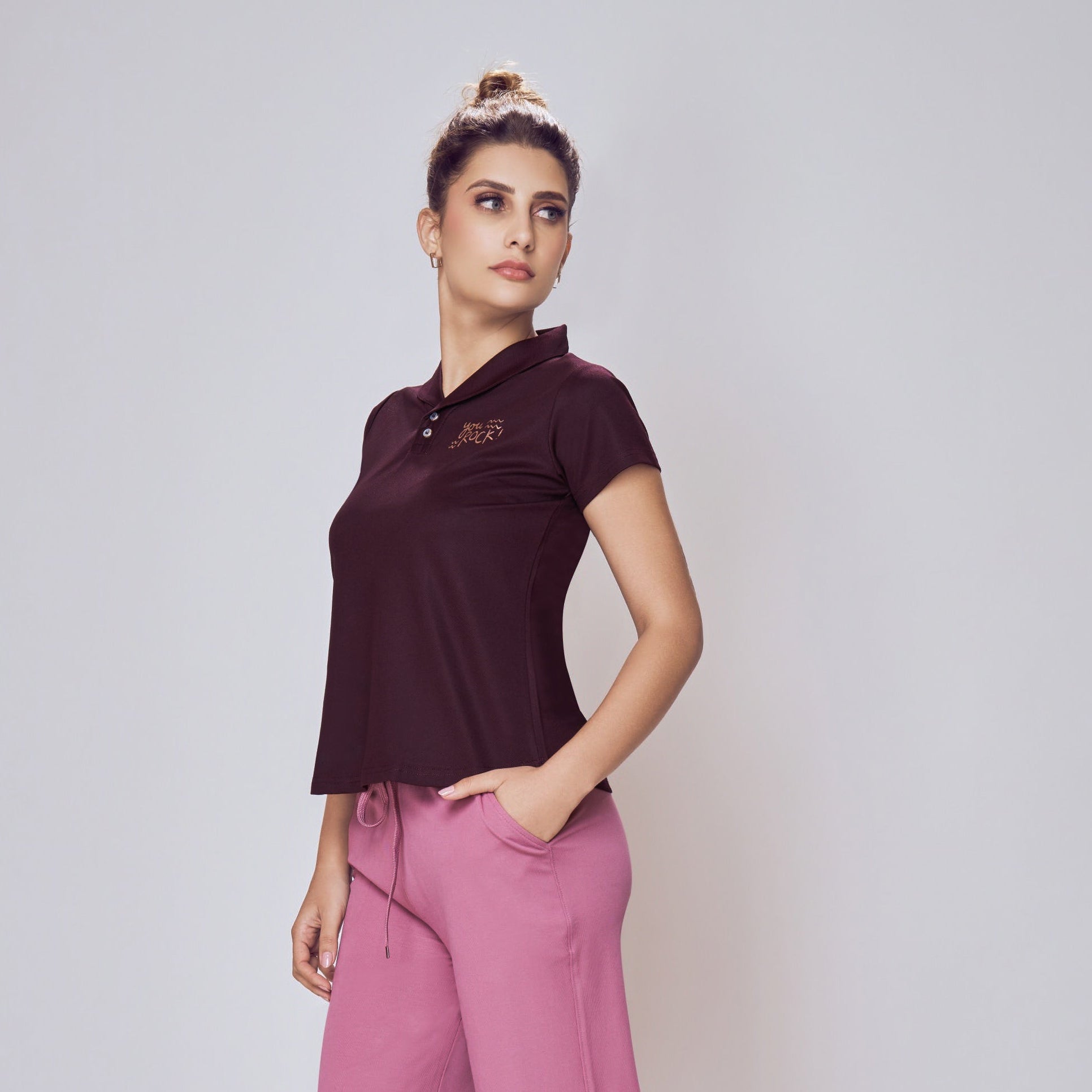 Woman wearing a dark purple polo shirt and pink pants on a white background