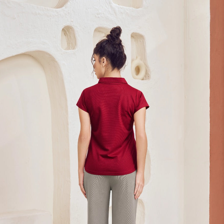 Person wearing a red shirt and gray pants standing in a room with a textured wall and white rug.