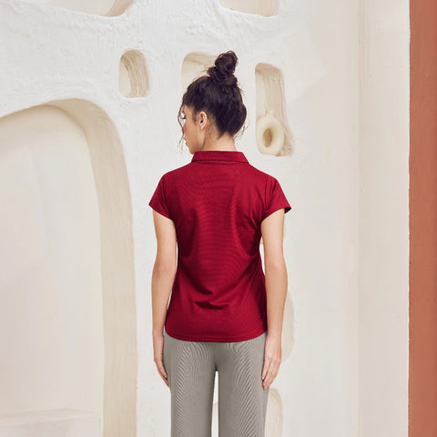 Person wearing a red shirt and gray pants standing in a room with a textured wall and white rug.
