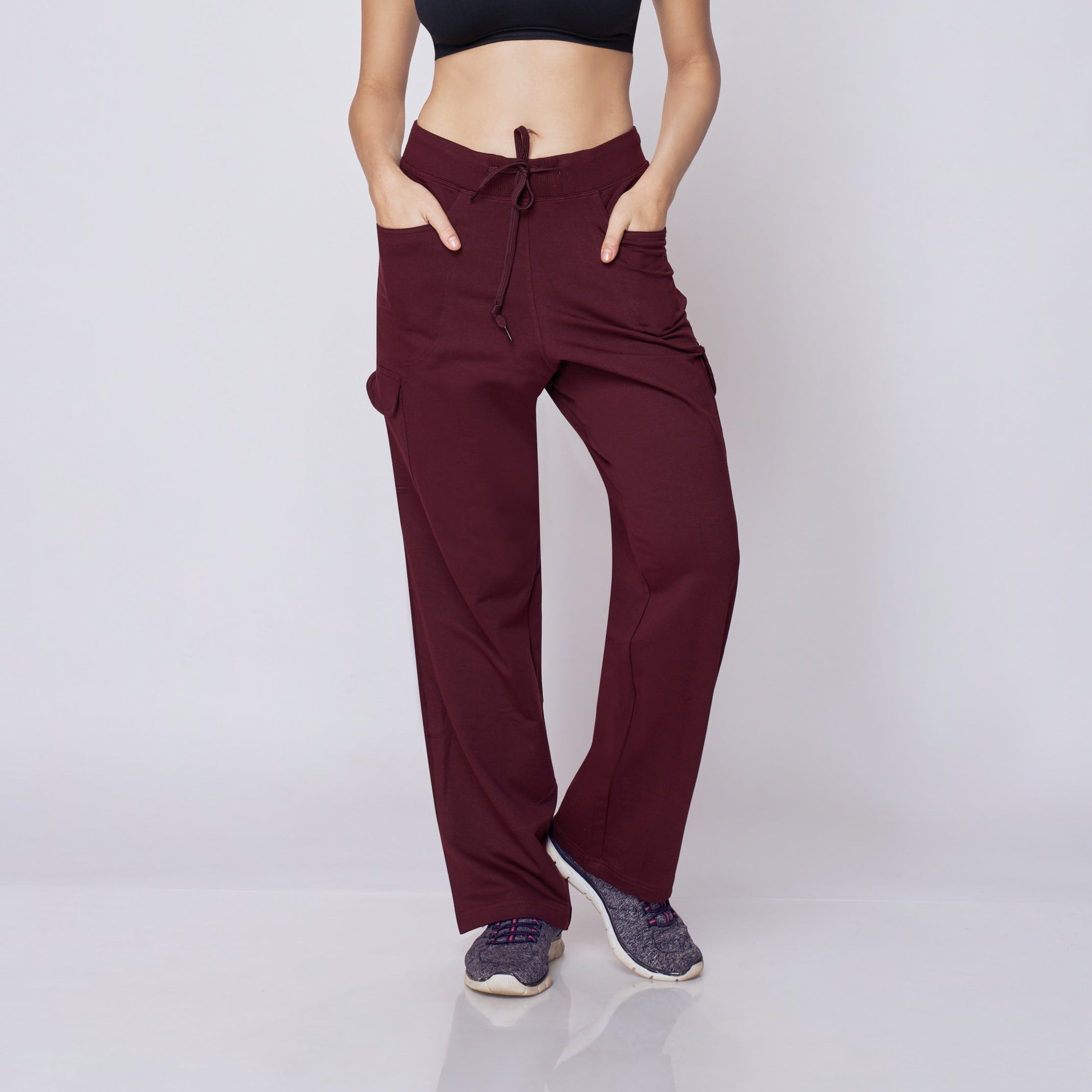 Woman wearing a black sports bra and maroon Essential Cargo Pants pants on a white background