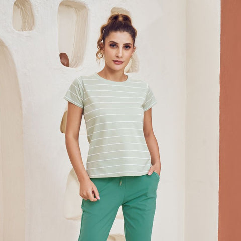 Woman wearing a striped shirt and green pants in a minimalistic room.