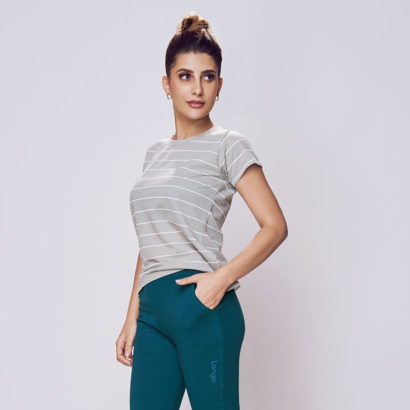 Woman wearing teal pants and a gray striped shirt on a white background