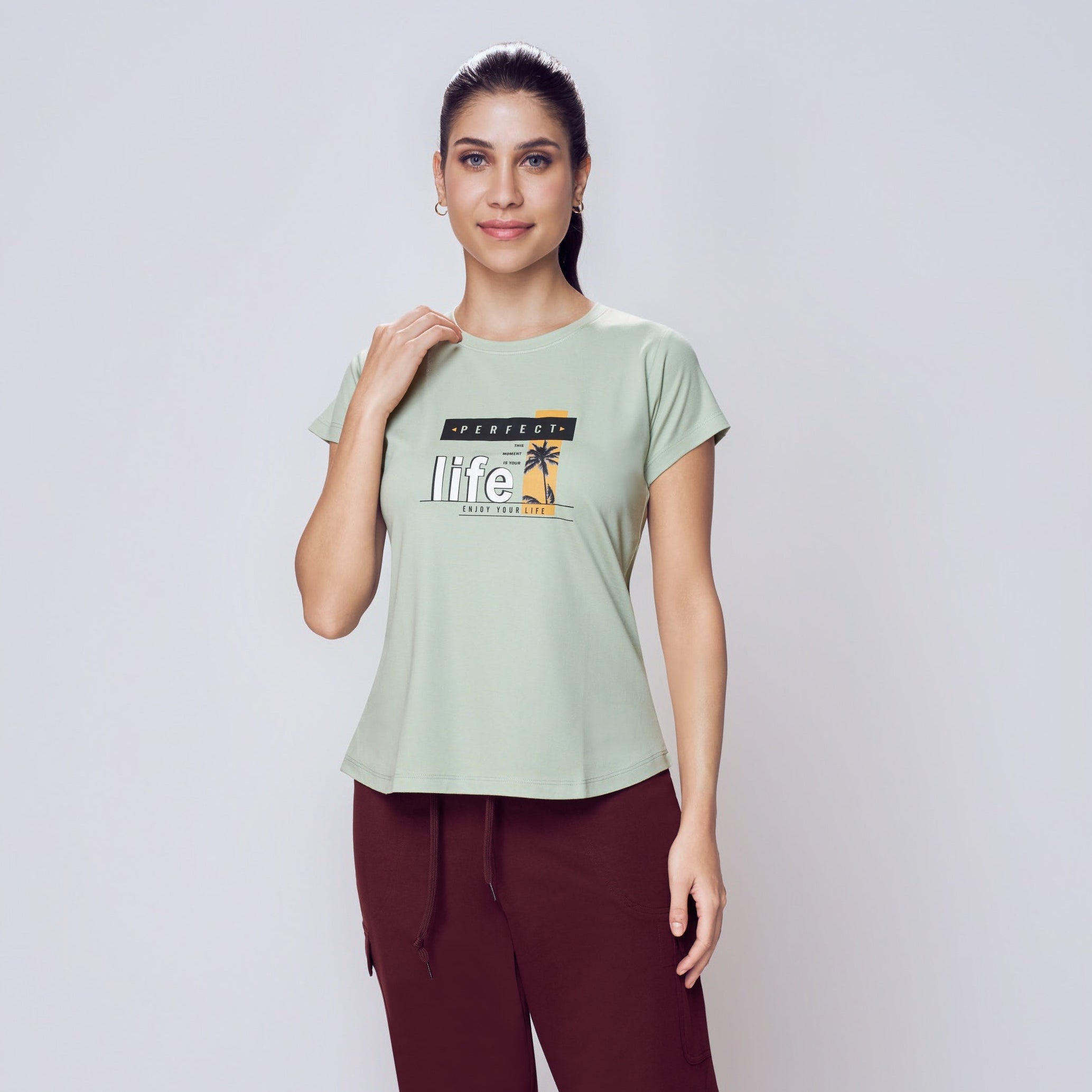 Woman wearing a light green t-shirt with text and maroon pants on a white background