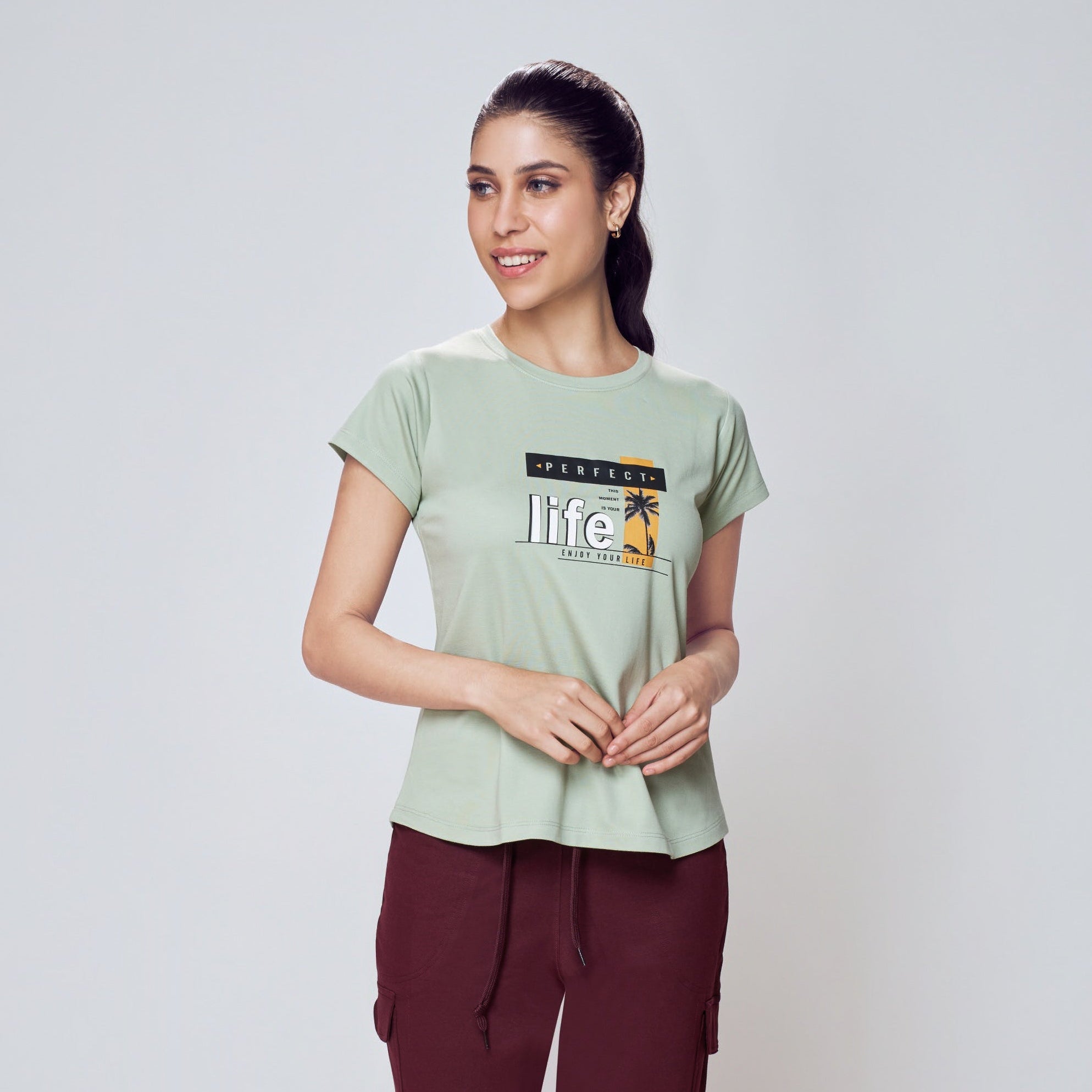 Woman wearing a light green t-shirt with text and maroon pants on a white background