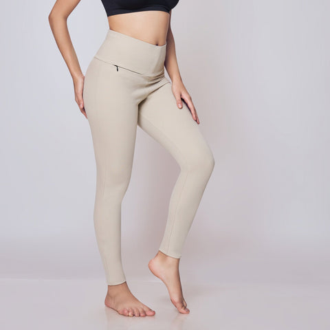 Woman wearing a black sports bra and beige leggings on a white background