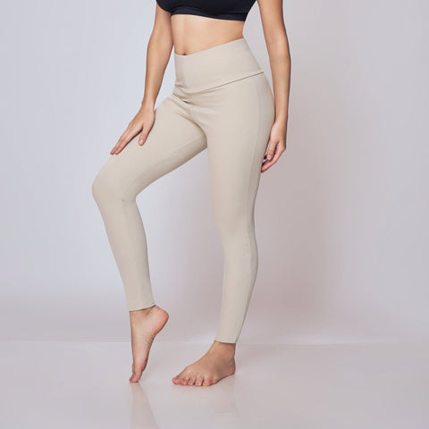 Woman wearing a black sports bra and beige leggings on a white background