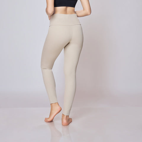 Woman wearing a black bra and beige leggings on a white background