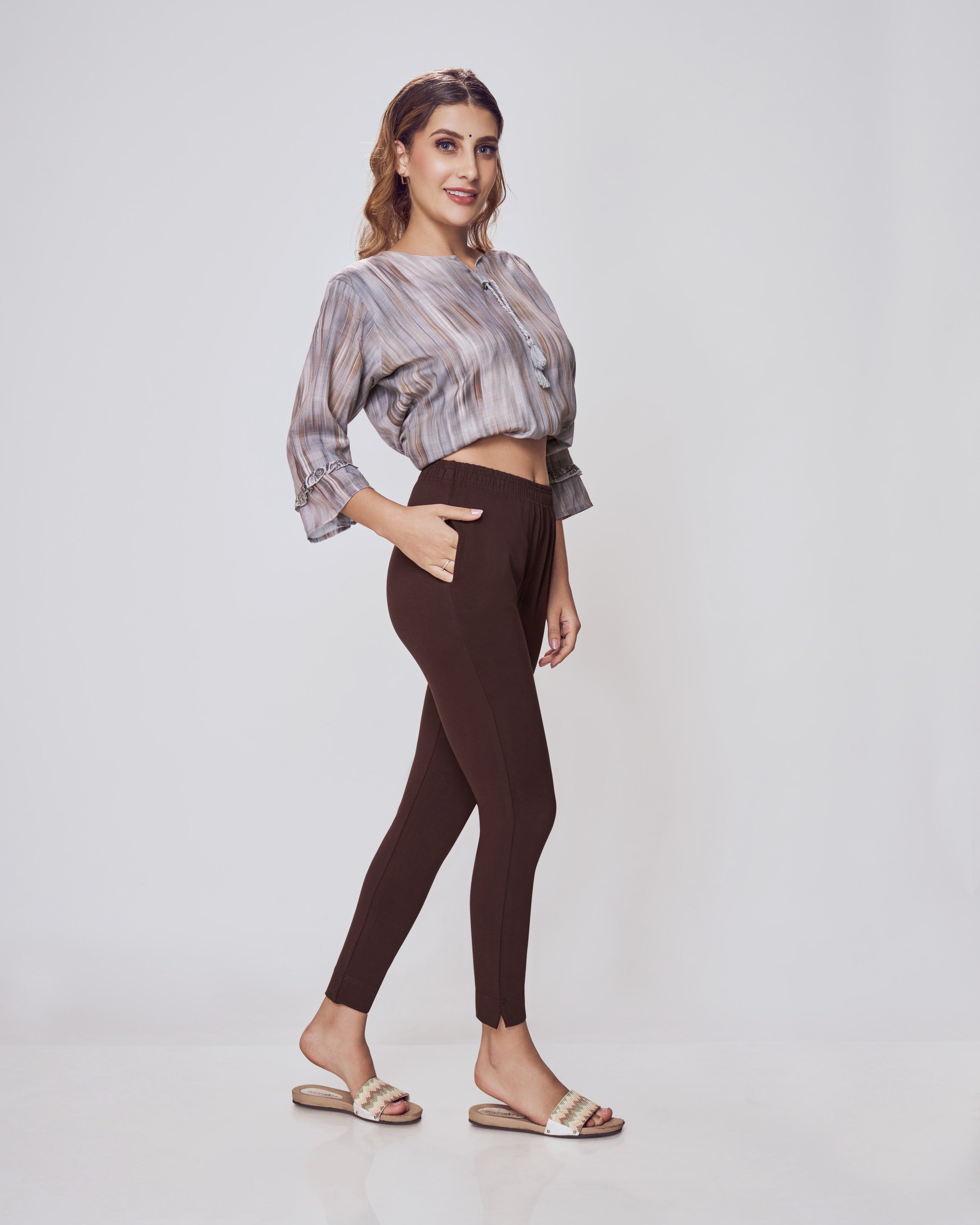 Woman wearing a patterned top and brown pants on a white background