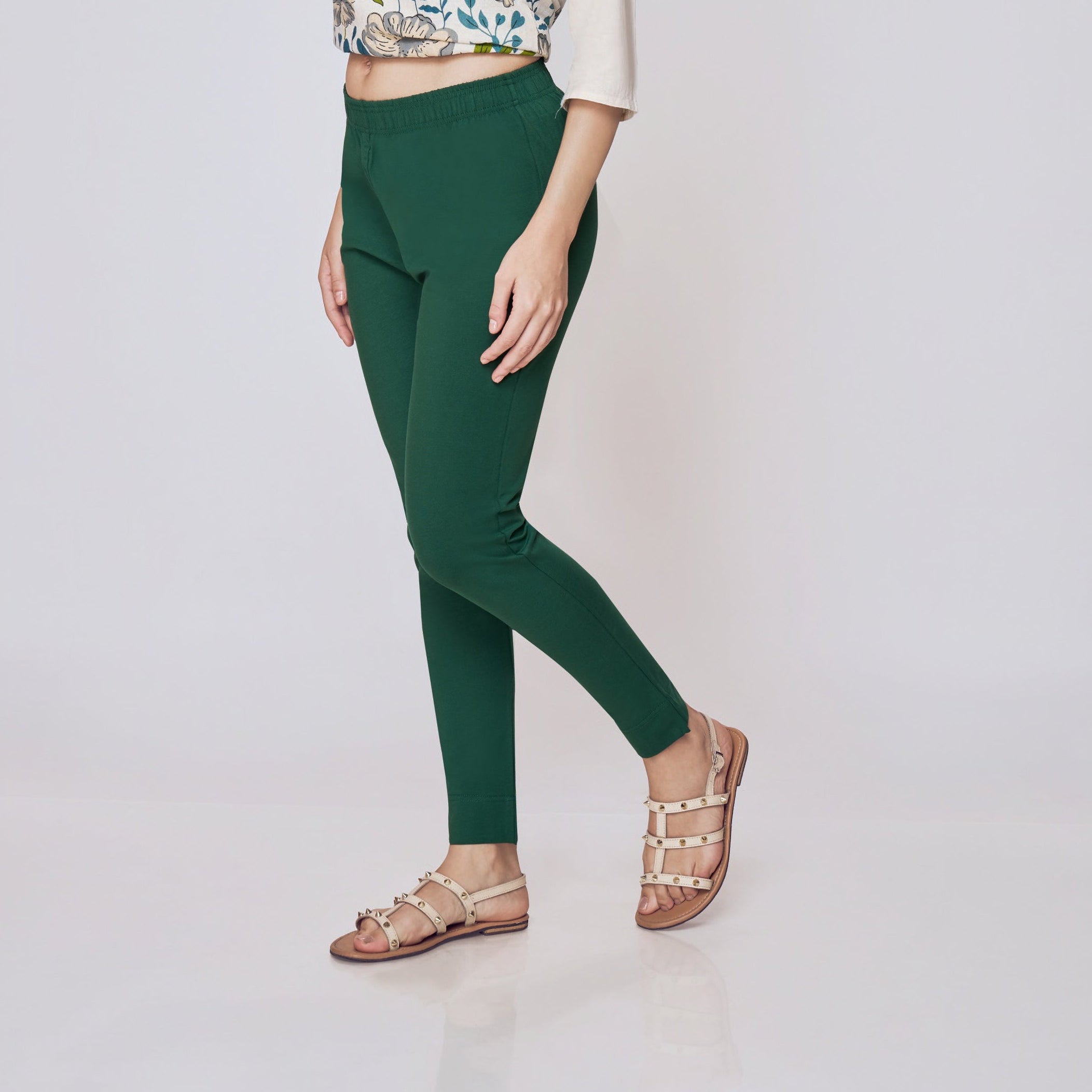 Woman wearing a cream top with floral design and green pants on a white background