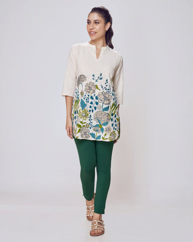 Woman wearing a beige blouse with floral patterns and green pants on a white background