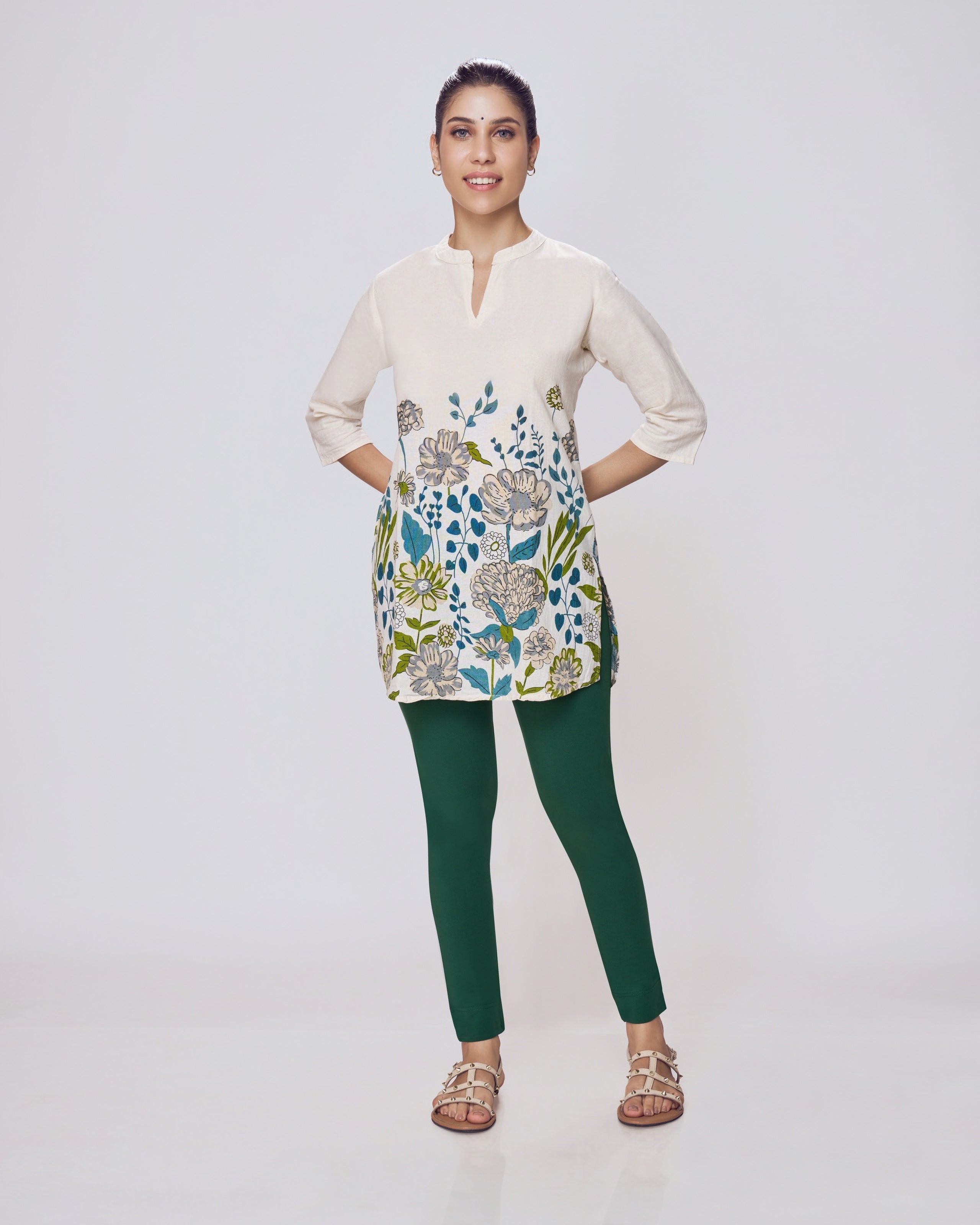 Woman wearing a floral dress over a beige shirt with green pants on a white background