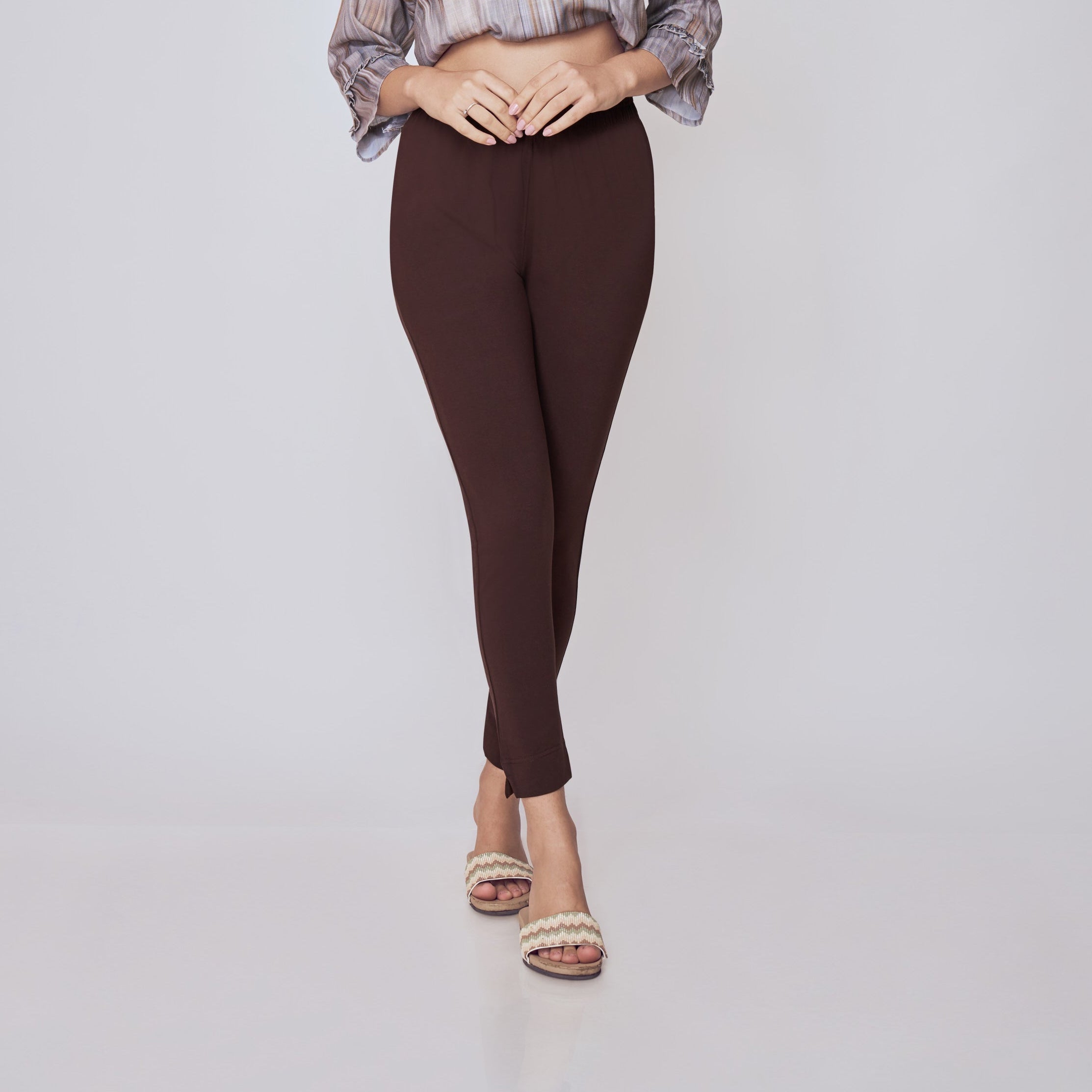 Woman wearing a patterned top and dark pants on a white background