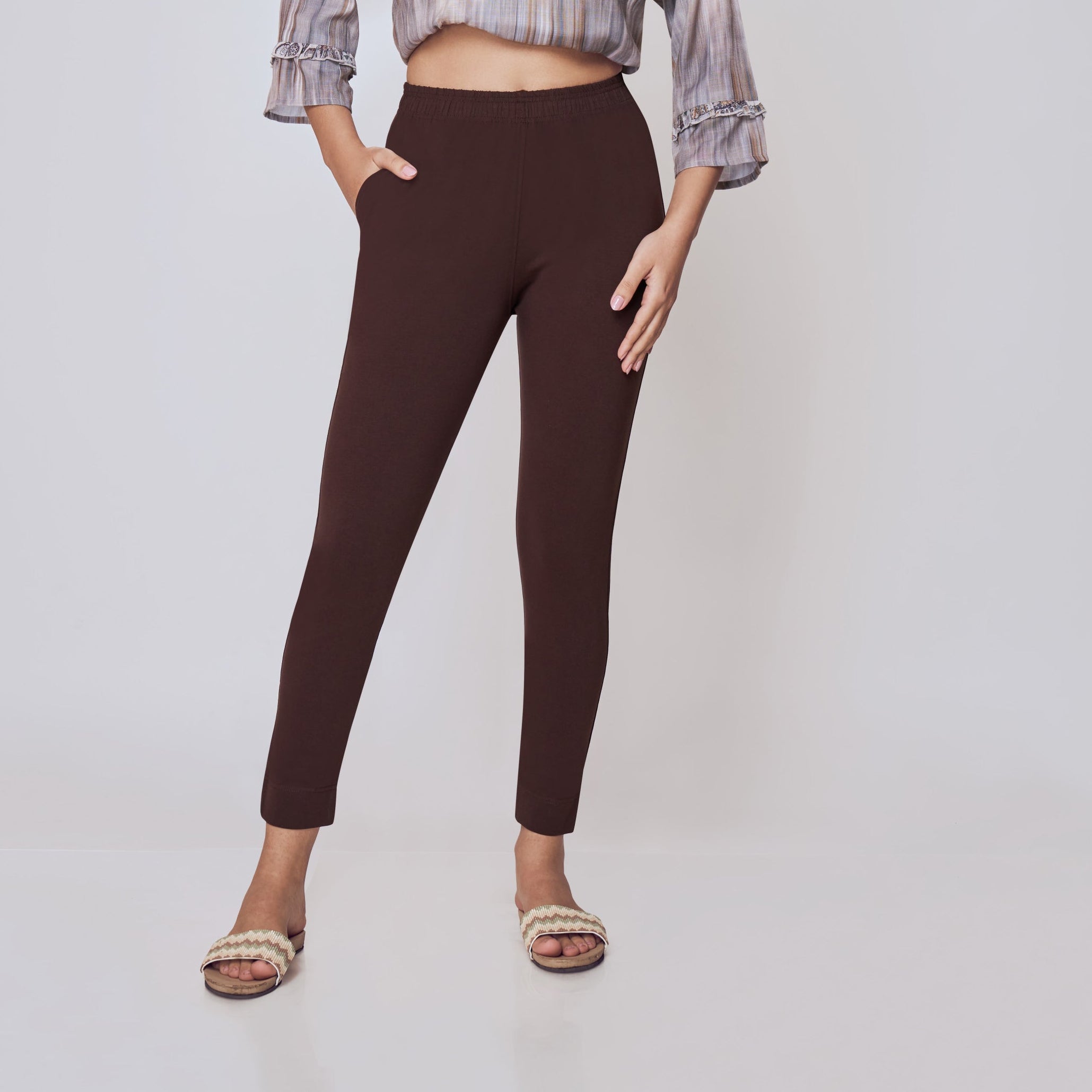Woman wearing a patterned top and brown pants on a white background