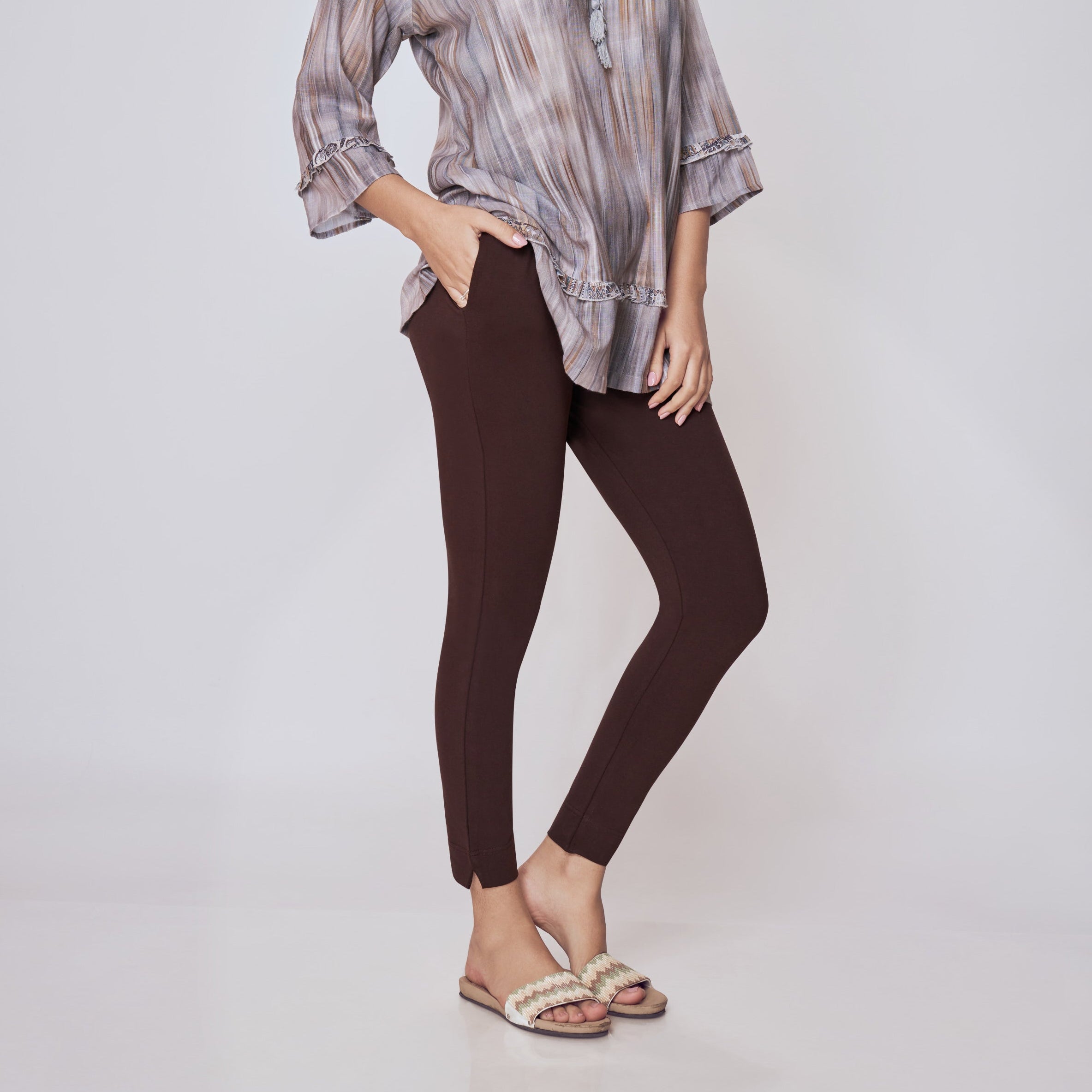 Woman wearing a patterned shirt and brown pants on a white background