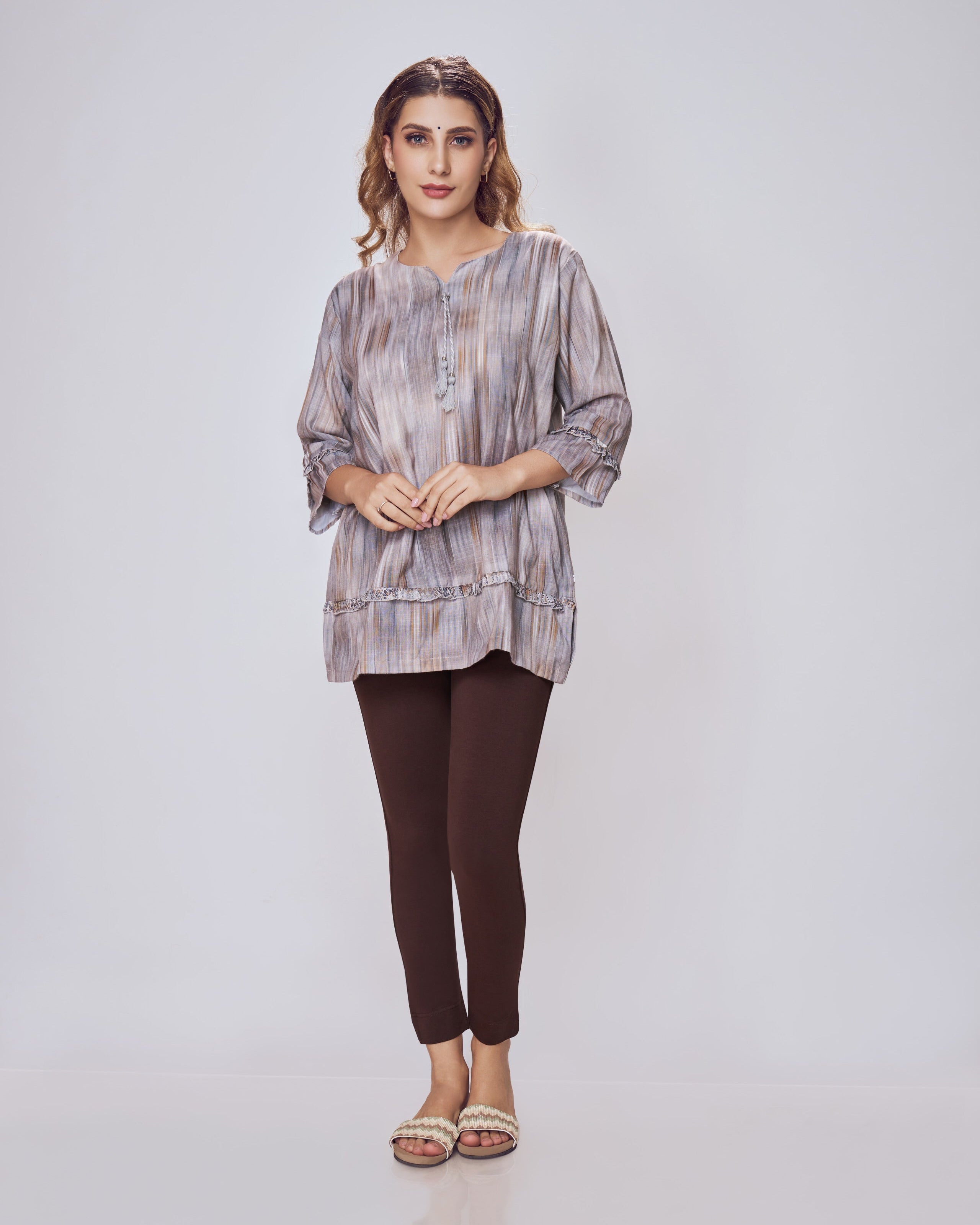 Woman wearing a patterned top and dark pants on a white background