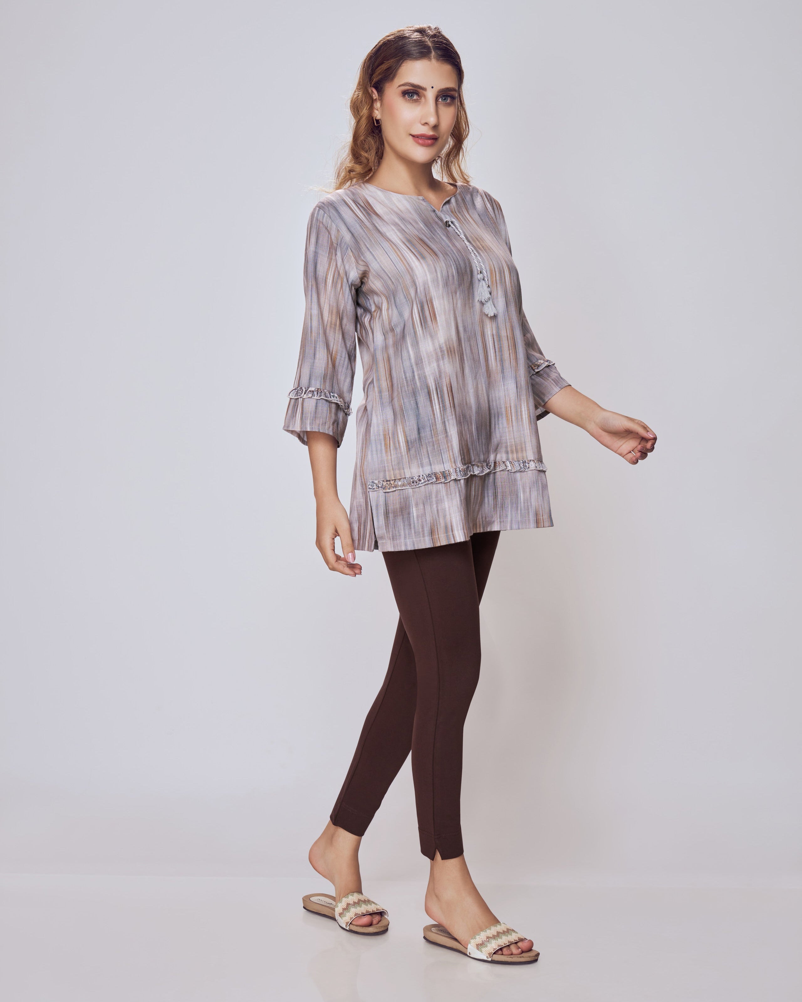 Woman wearing a patterned top and dark leggings on a white background