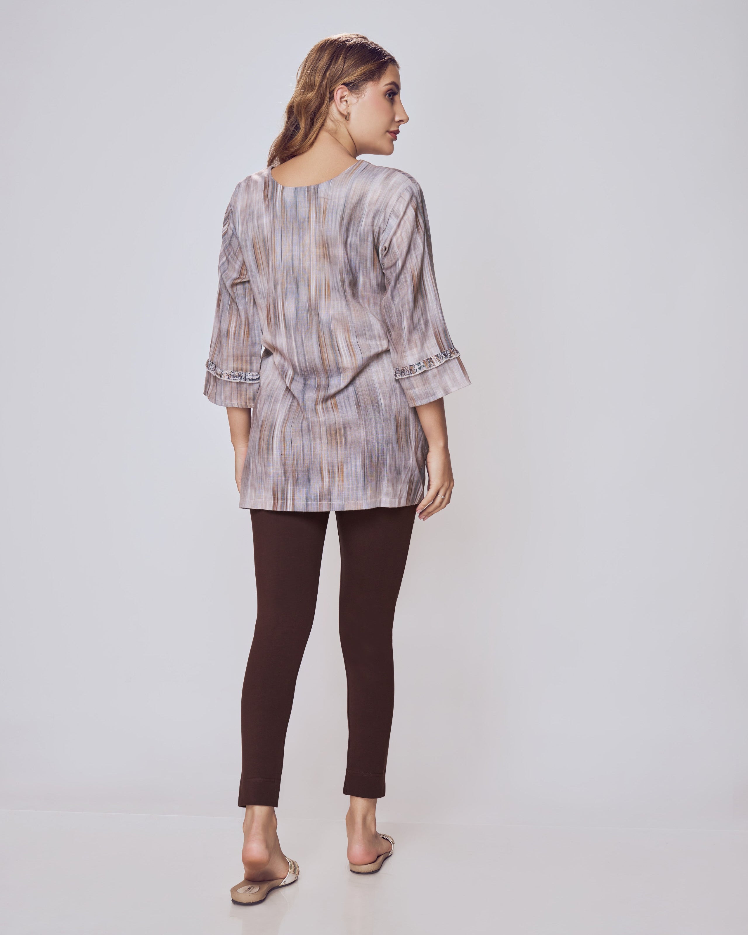 Woman wearing a patterned shirt and dark pants on a white background