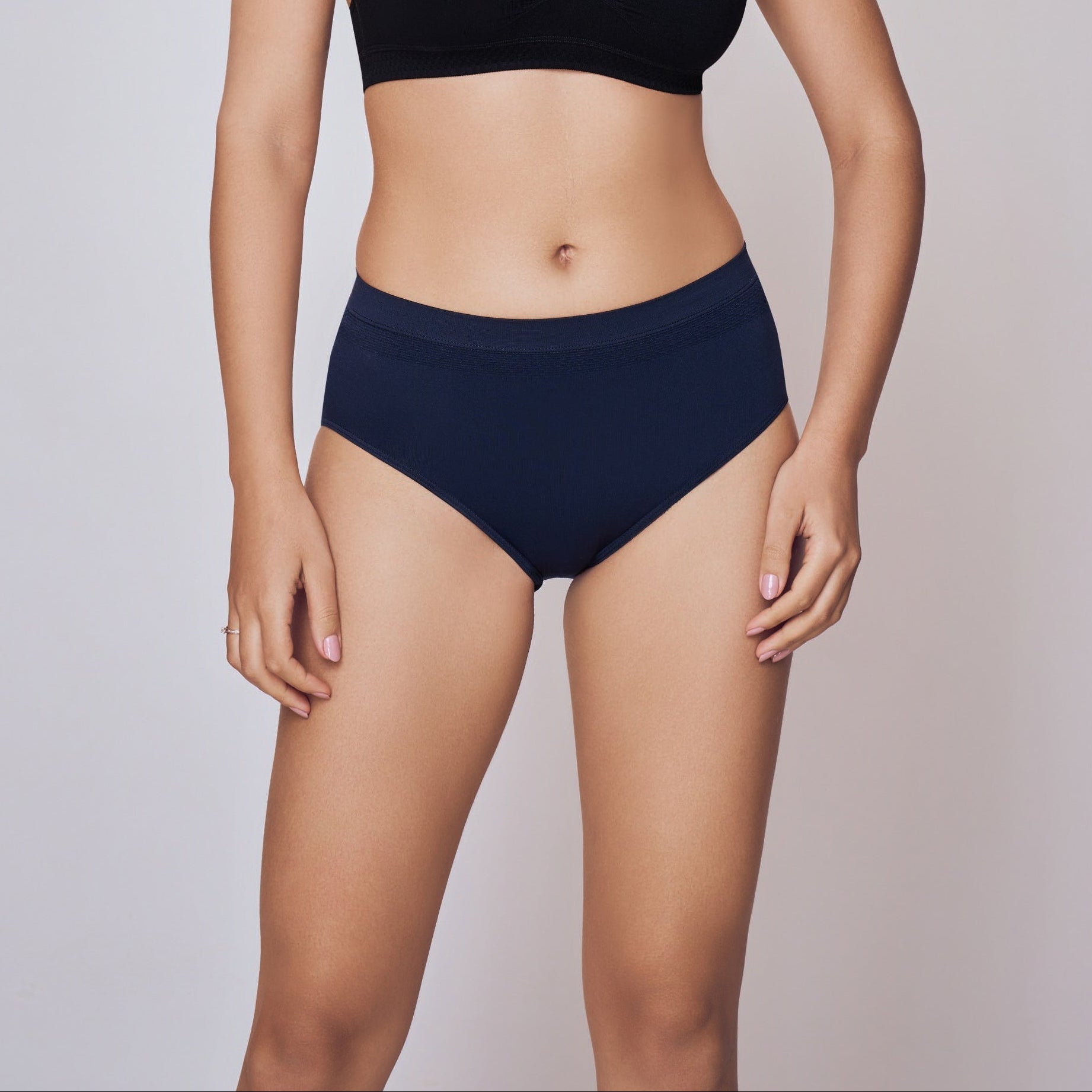 Woman wearing a black sports bra and navy blue Lady Care Air V Hipster Panty Pack - Pack of 3 bottom on a gray background