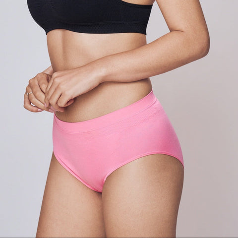 Woman wearing a black sports bra and pink Lady Care Air V Hipster Panty on a gray background