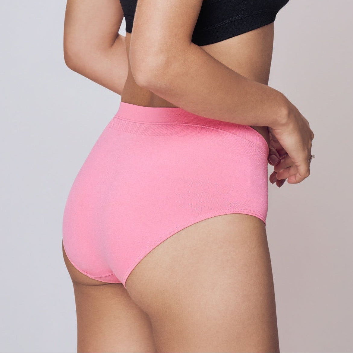 Woman wearing a black sports bra and pink  Lady Care Air V Hipster Panty on a plain background