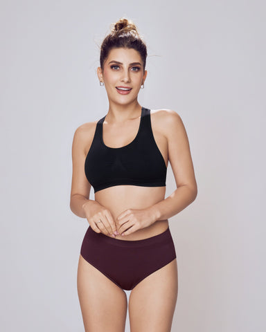 Woman wearing a black sports bra and maroon high-waisted bikini bottom on a gray background
